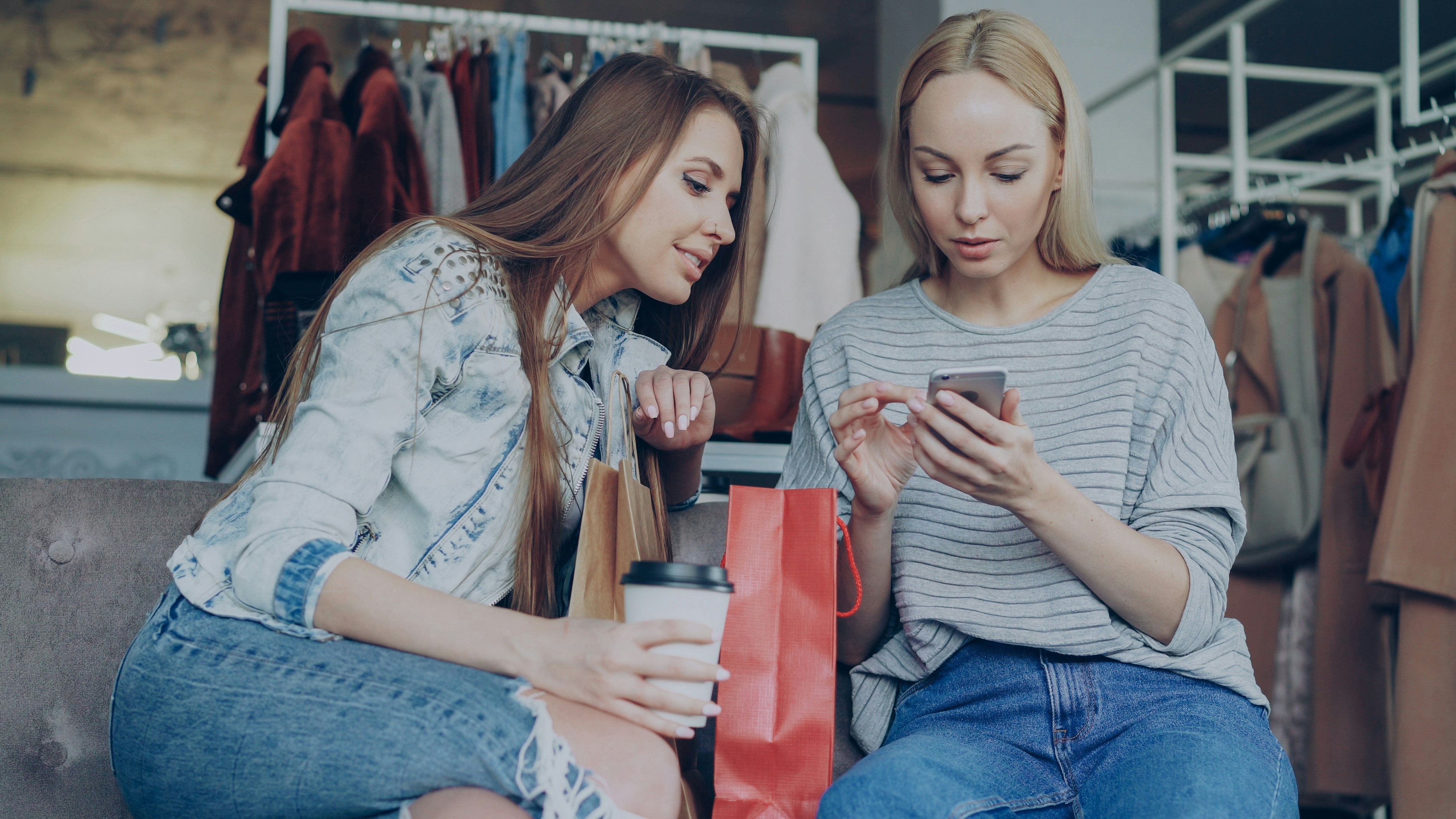 Two friends are looking at a phone in a boutique.