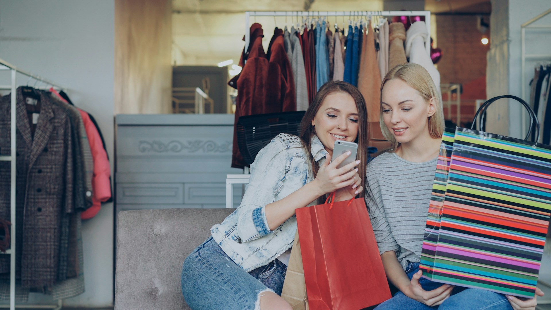 Two women are shopping and looking at a phone.