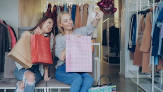 Two friends pose for a selfie with shopping bags.