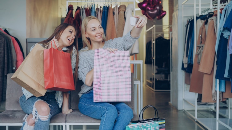 Two friends pose for a selfie with shopping bags.