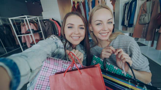 Two women smile with shopping bags in a store.