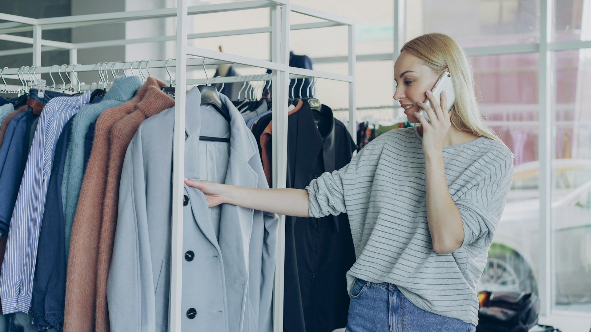 A woman looks at clothes while on the phone.