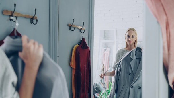 Woman picks a coat in front of a mirror.