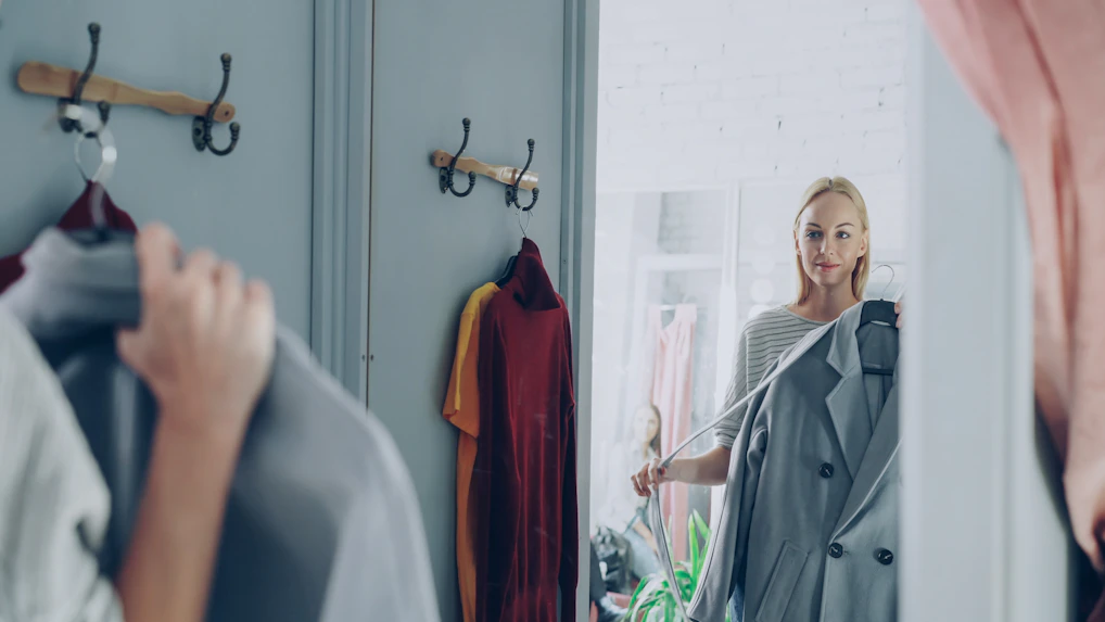 Woman picks a coat in front of a mirror