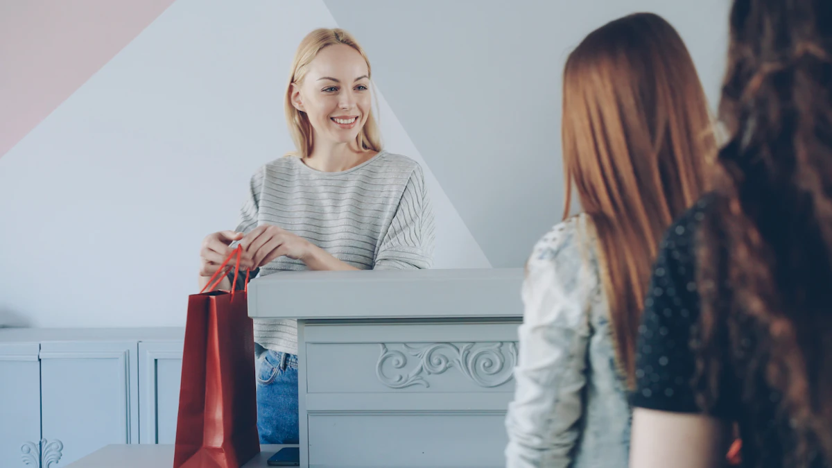 Une vendeuse souriante en pull gris tend un sac en papier rouge par-dessus un comptoir blanc à deux clientes vues de dos