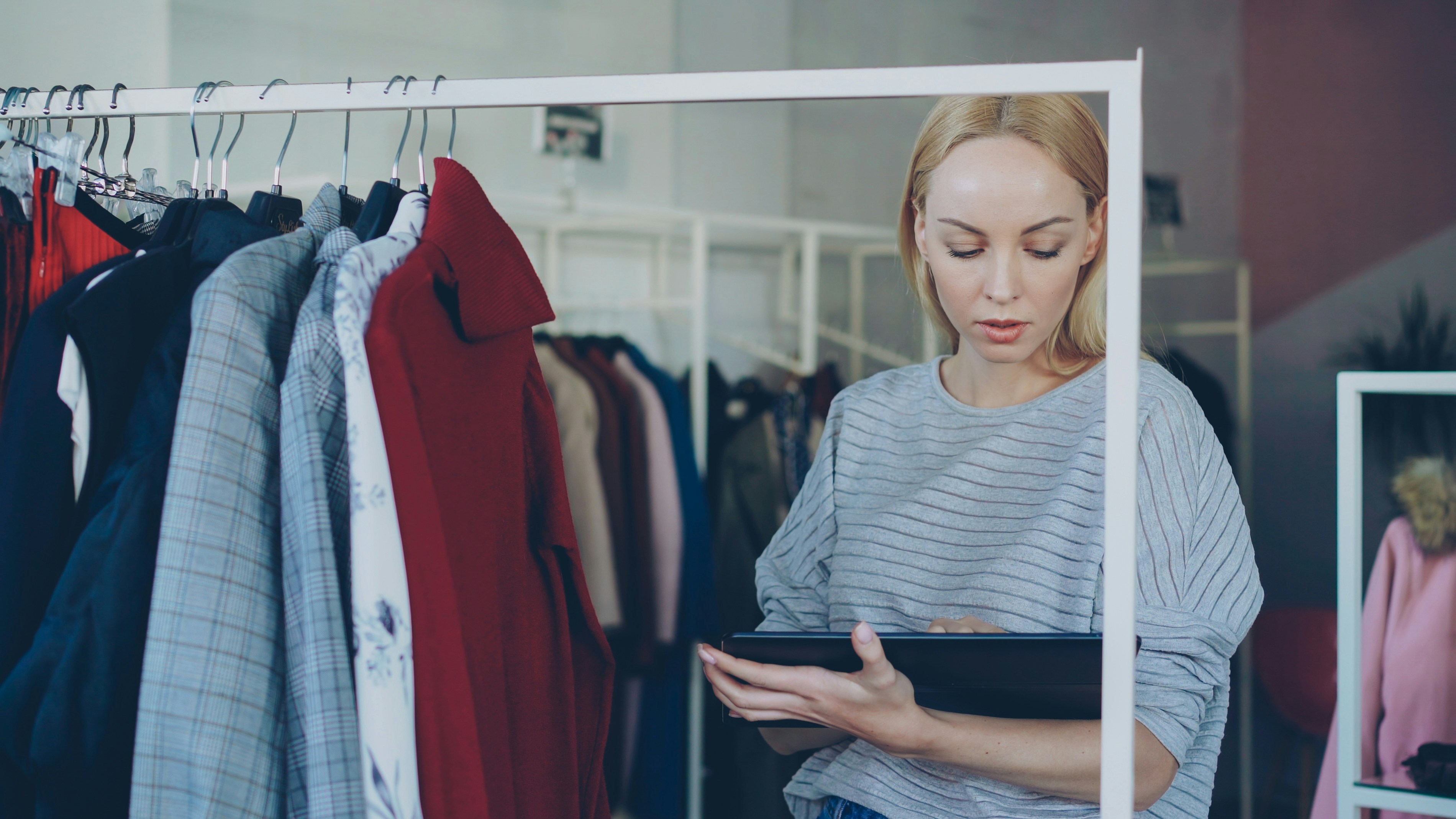 Young businesswoman is checking garments on rails and working with tablet in her clothing shop