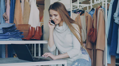 Woman talks on the phone while using a laptop.