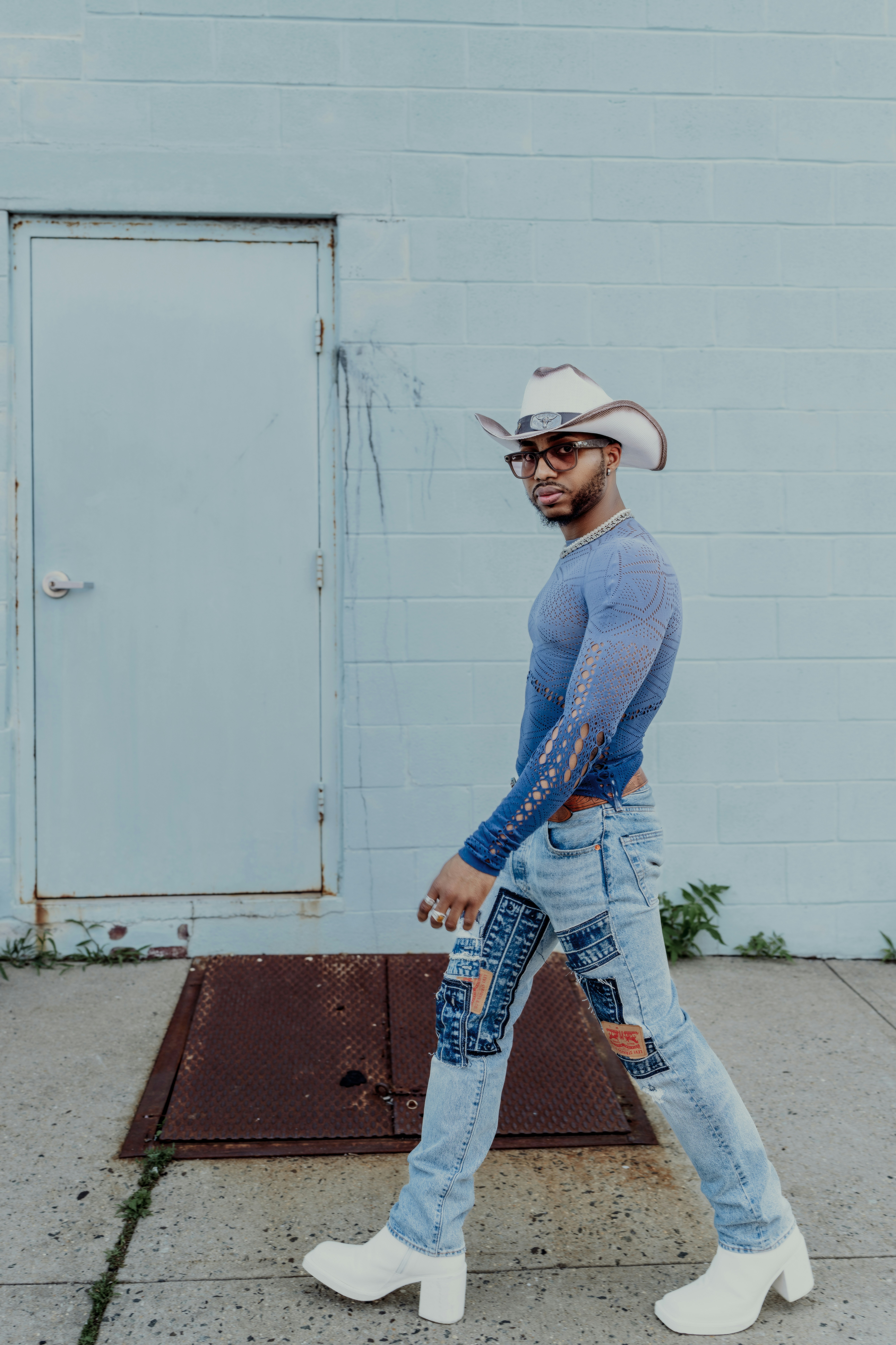 A person in a cowboy hat walks by a blue wall.