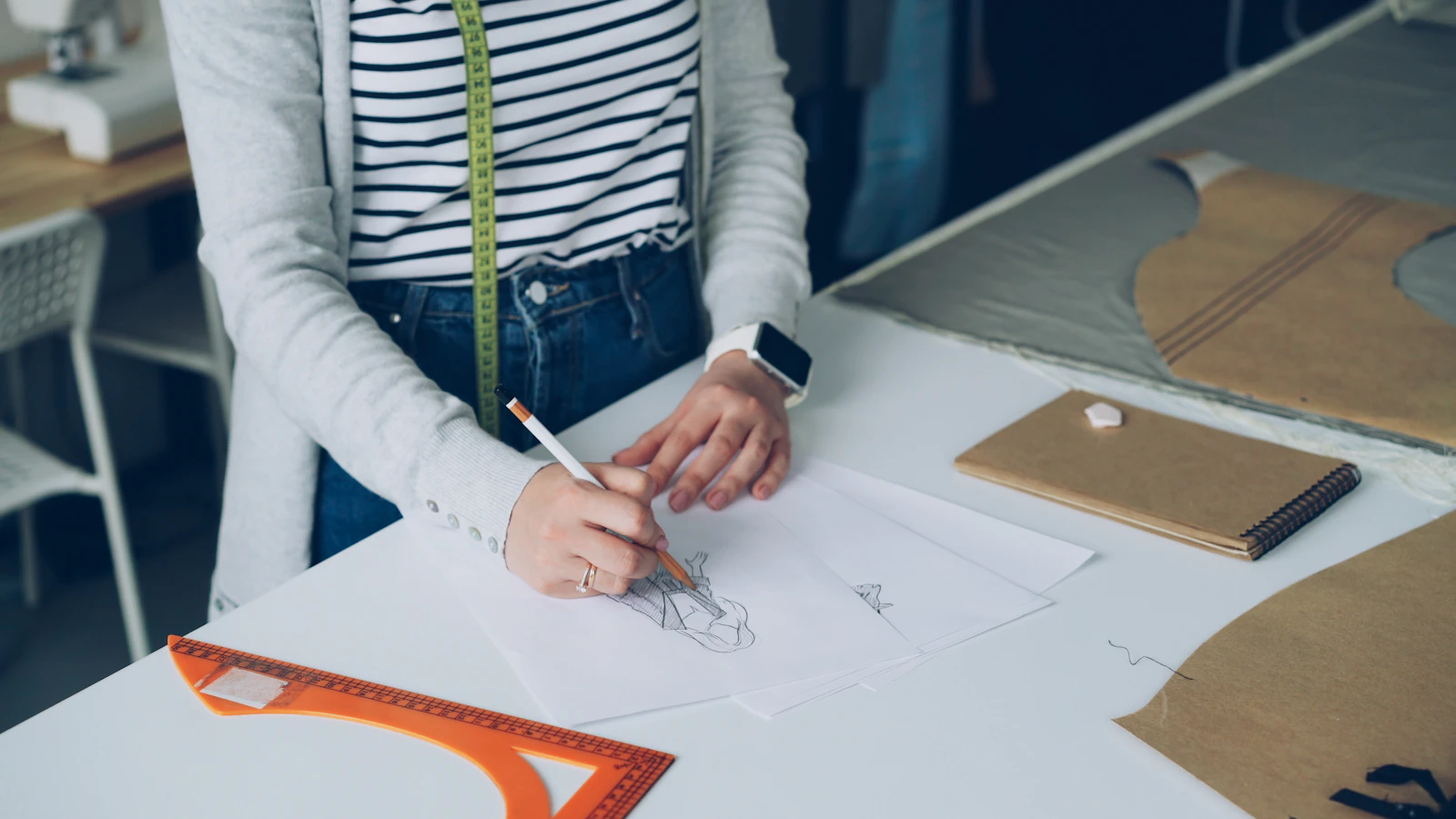 A fashion designer sketching a garment design on paper with a pencil at her studio desk