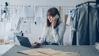 Fashion designer works on laptop while talking on phone.