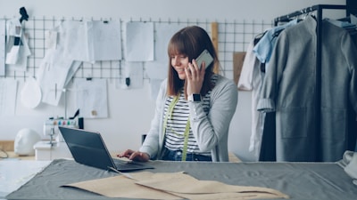 Fashion designer works on laptop while talking on phone.