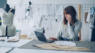 Fashion designer works on laptop while talking on the phone.