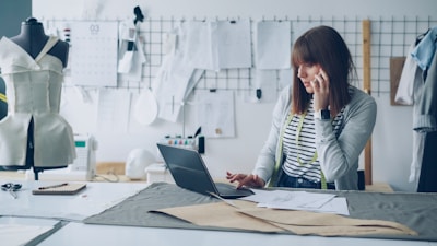 Fashion designer works on laptop while talking on the phone.