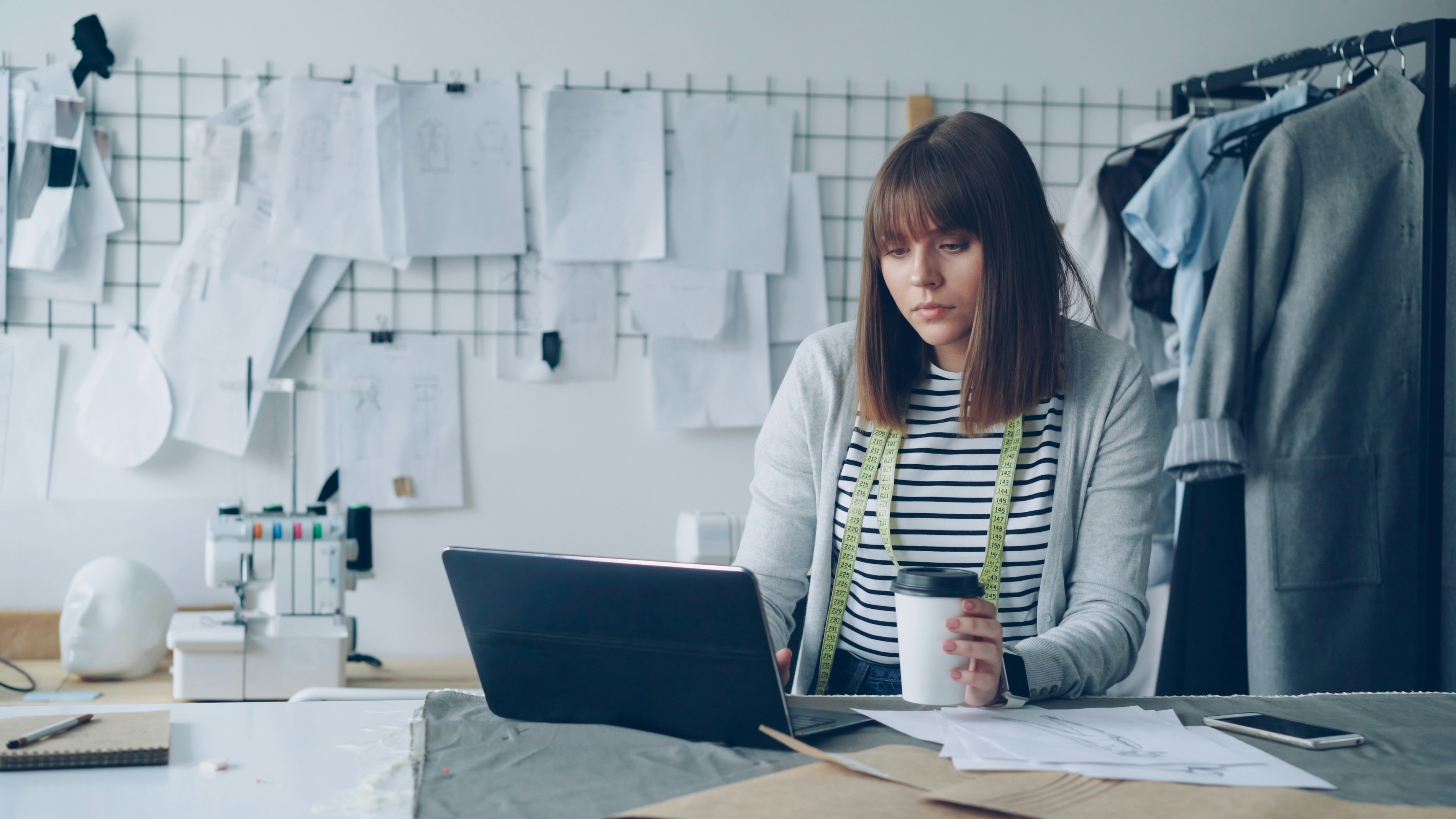 Young seamstress working on laptop with coffee