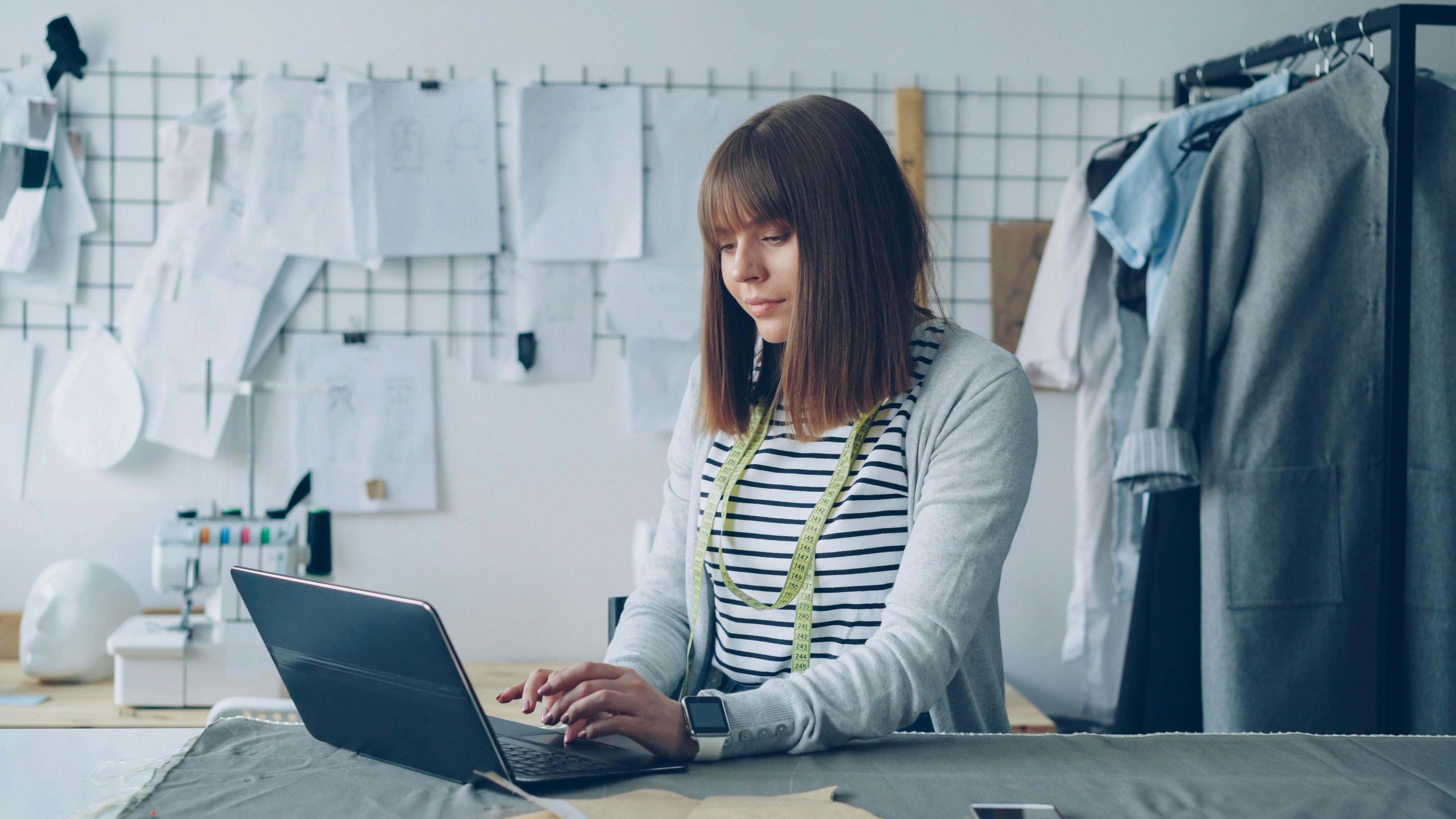 Young self-employed tailor is communicating with her customers using laptop