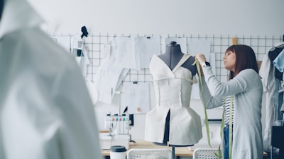A fashion designer measures a dress on a mannequin.