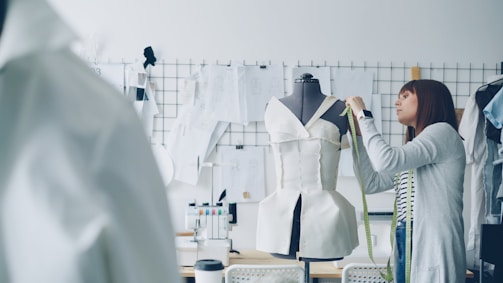 A fashion designer measures a dress on a mannequin.