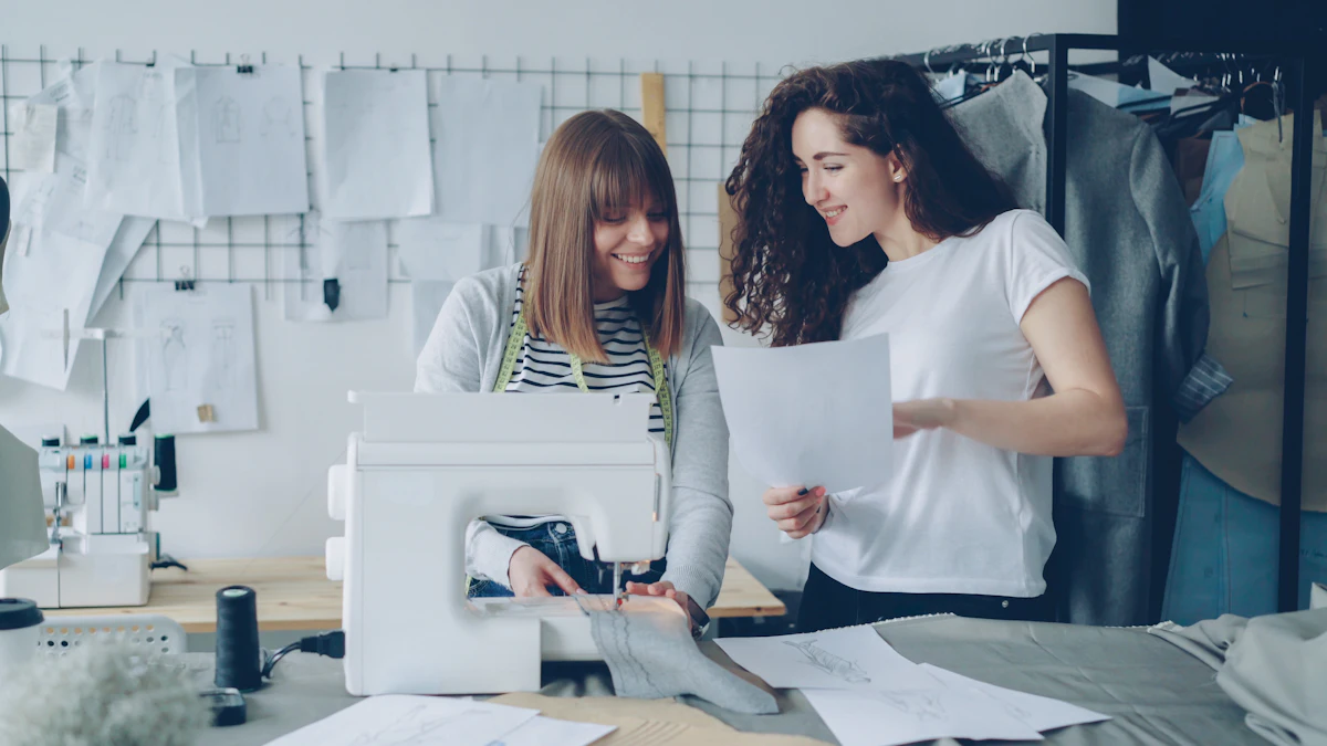 Two women working together in a studio — one at a sewing machine, the other holding sketches.