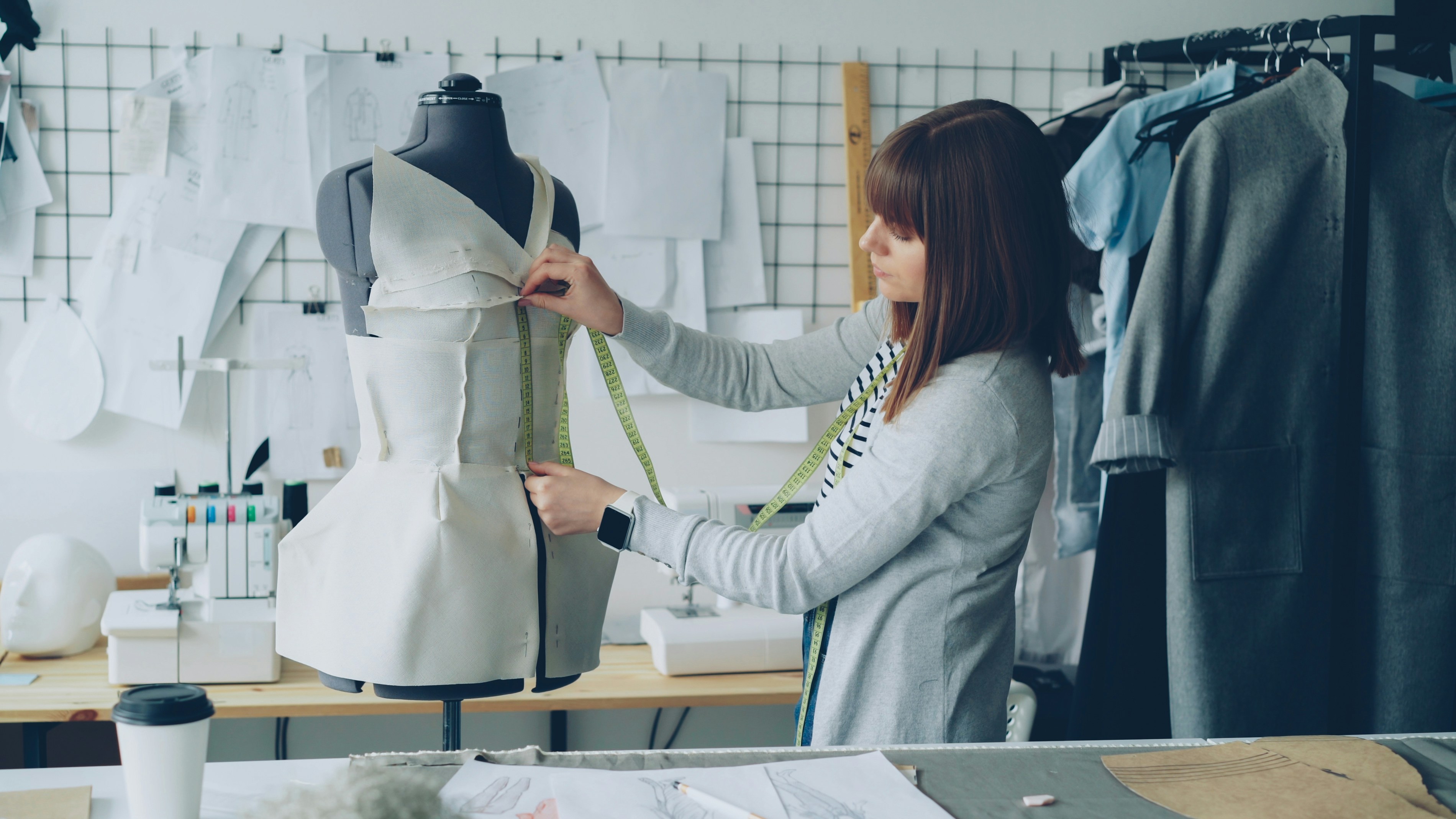 A fashion designer measures a garment on a mannequin.