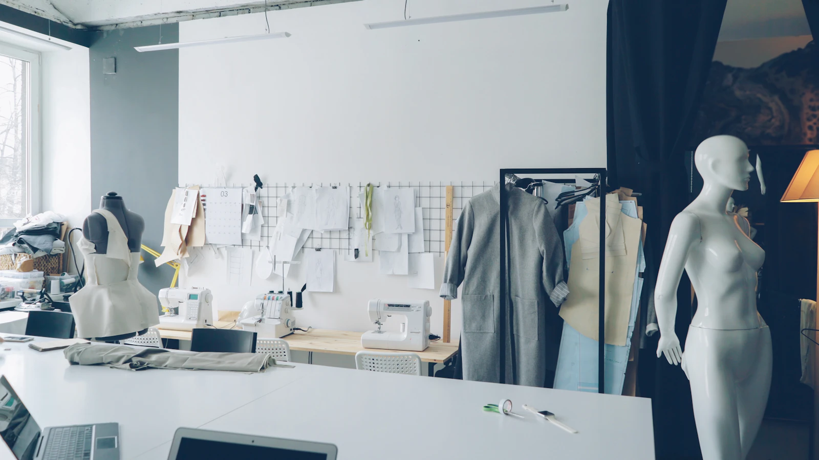 A small fashion design studio with a tailor's desk, mannequins, sewing machines and sketches