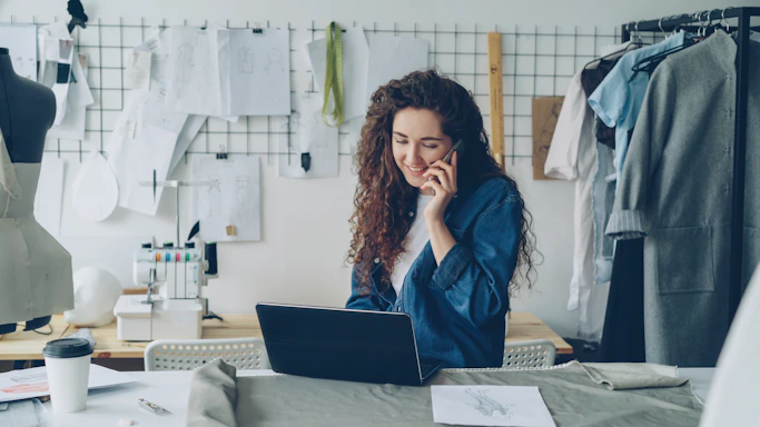 Fashion designer on the phone, working on a laptop.