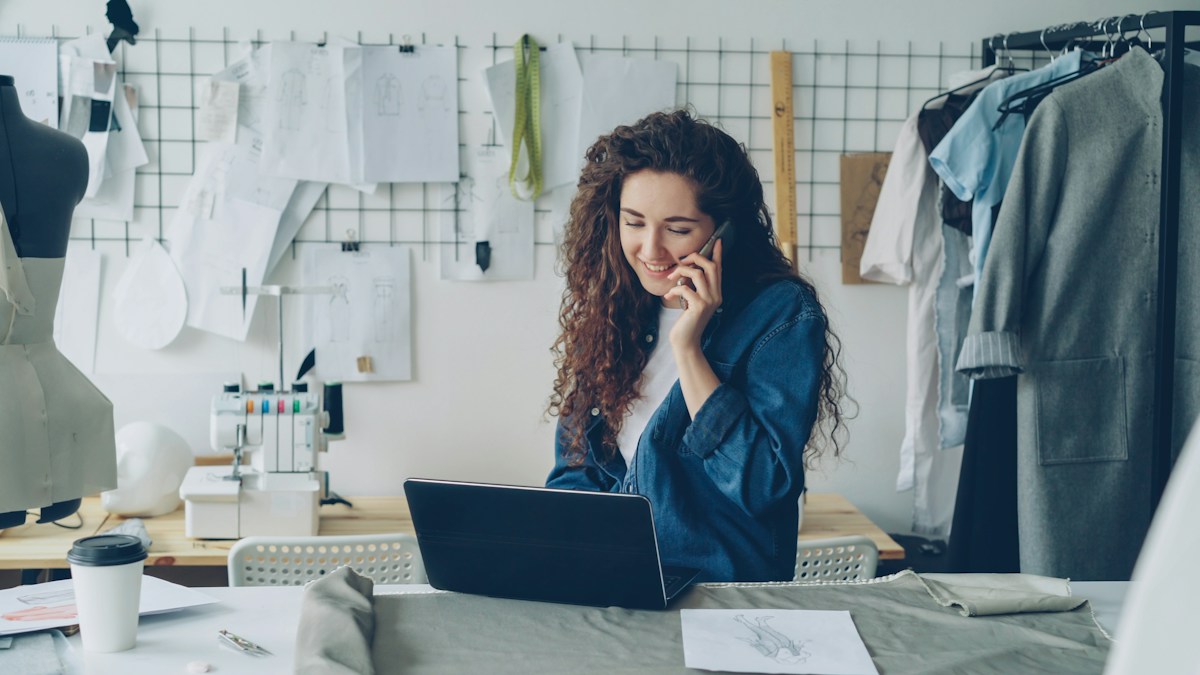 Small business owner multitasking on a phone and laptop in a warm-lit studio