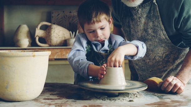 A boy learns pottery with help from an adult.