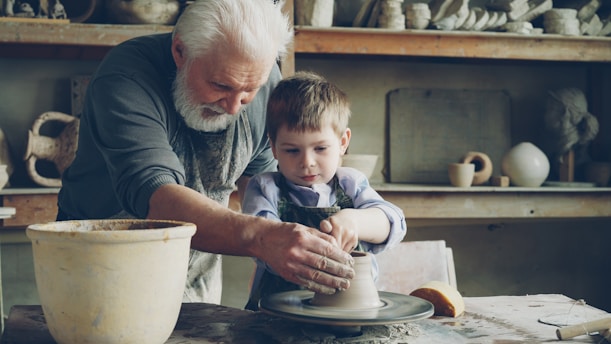 A grandfather teaches a child how to make pottery.