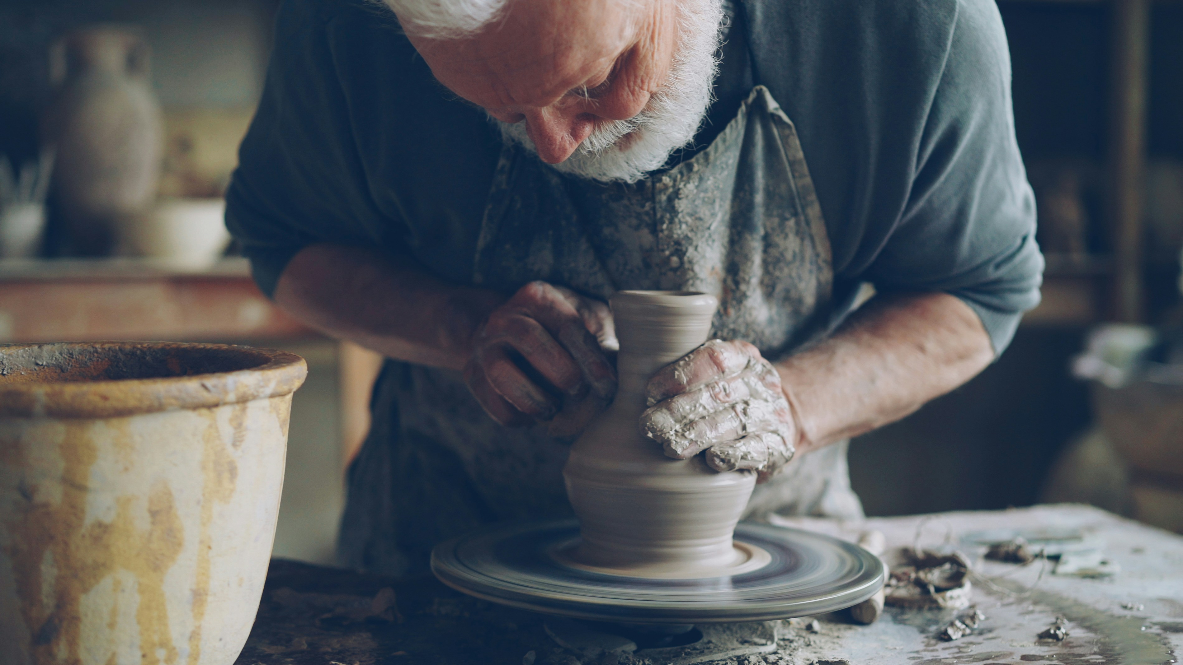 A potter shapes a clay vase on a spinning wheel.