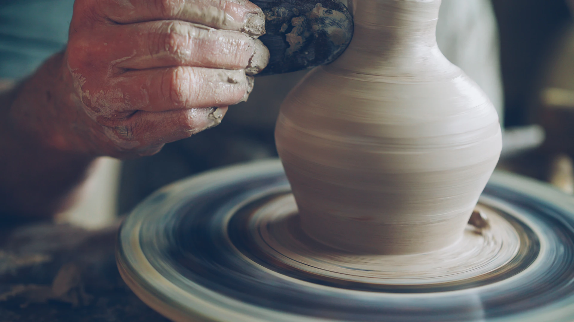 Potter shapes clay on a spinning wheel.