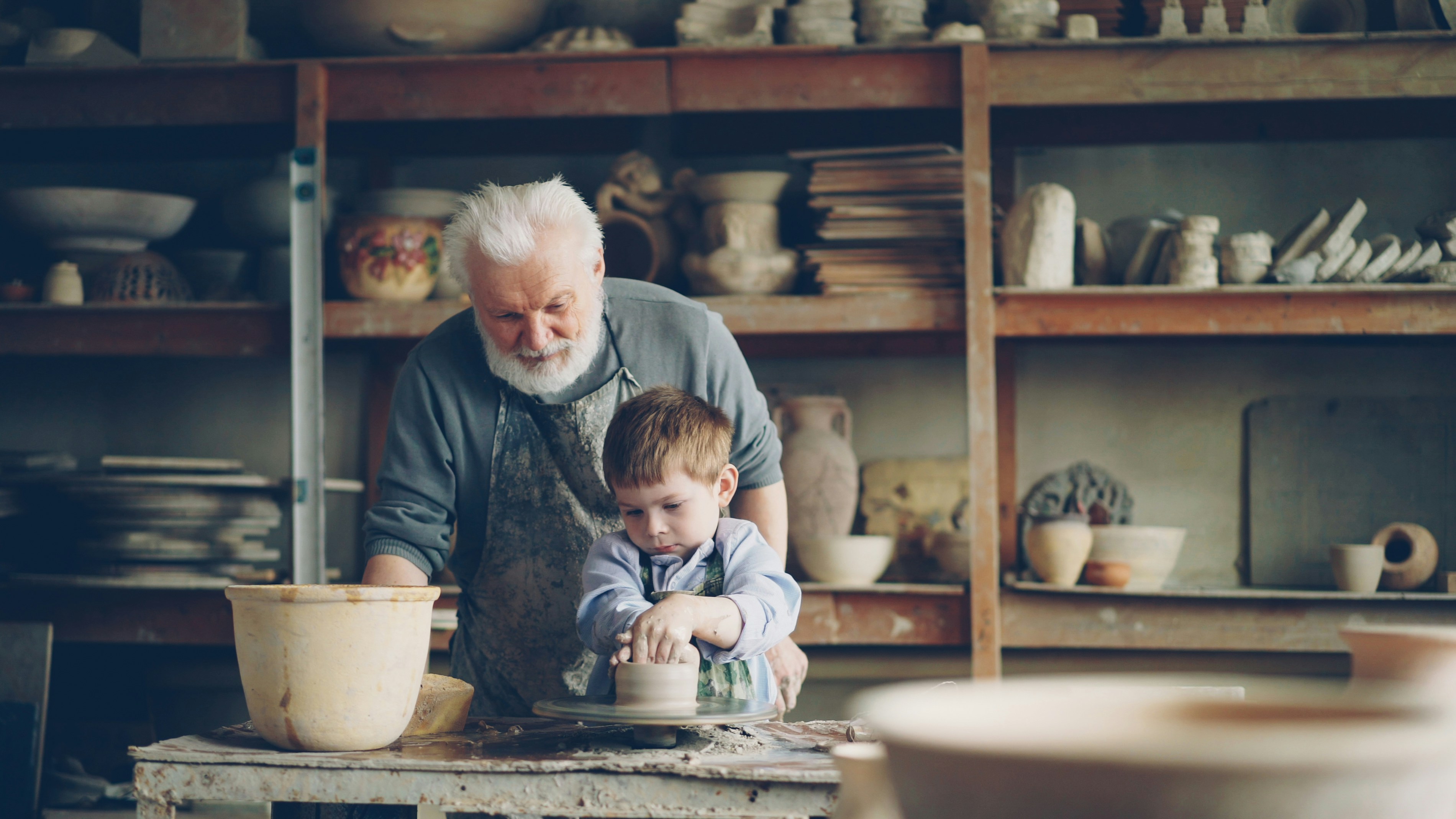 A grandfather teaches his grandson pottery.