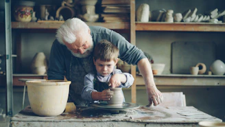 A grandfather teaches his grandson pottery.
