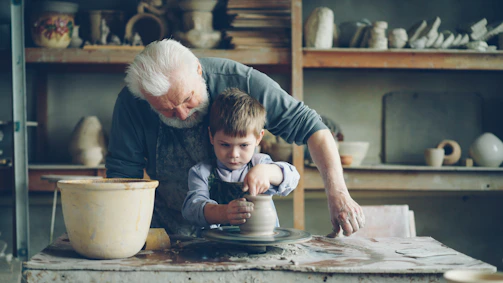 A grandfather teaches his grandson pottery.