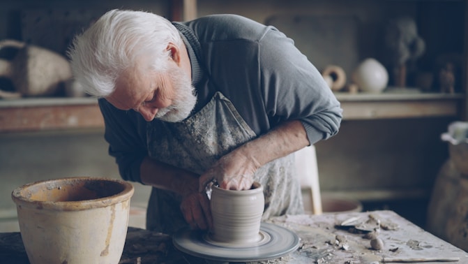 An older man is shaping clay on a wheel.