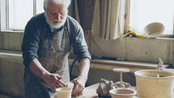 An old potter shapes clay in his workshop