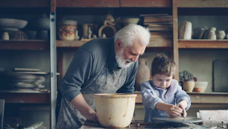 A grandfather teaches a boy pottery.