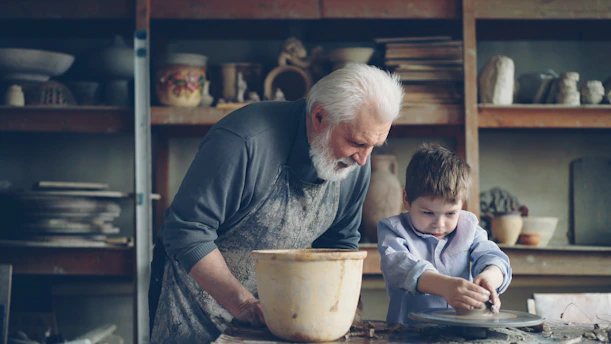 A grandfather teaches a boy pottery.