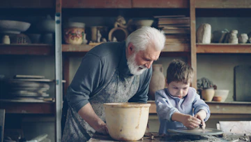 A grandfather teaches a boy pottery