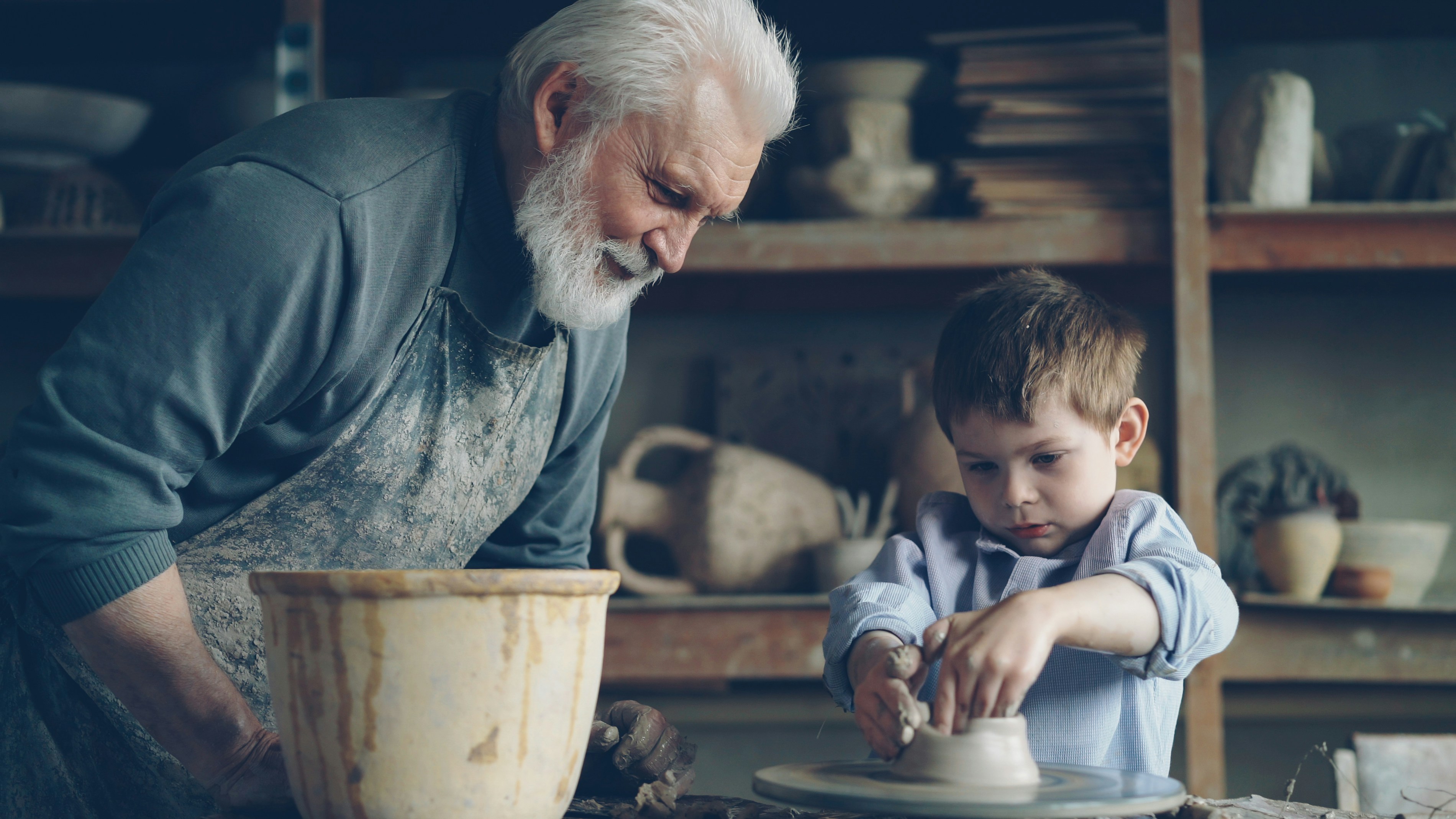 A grandfather shows his grandson how to make pottery.