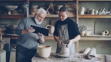 Potter guides a younger artist in his craft
