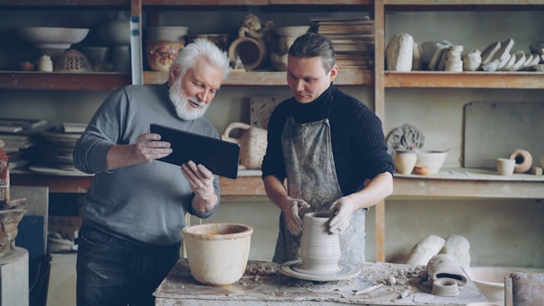 Potter guides a younger artist in his craft.