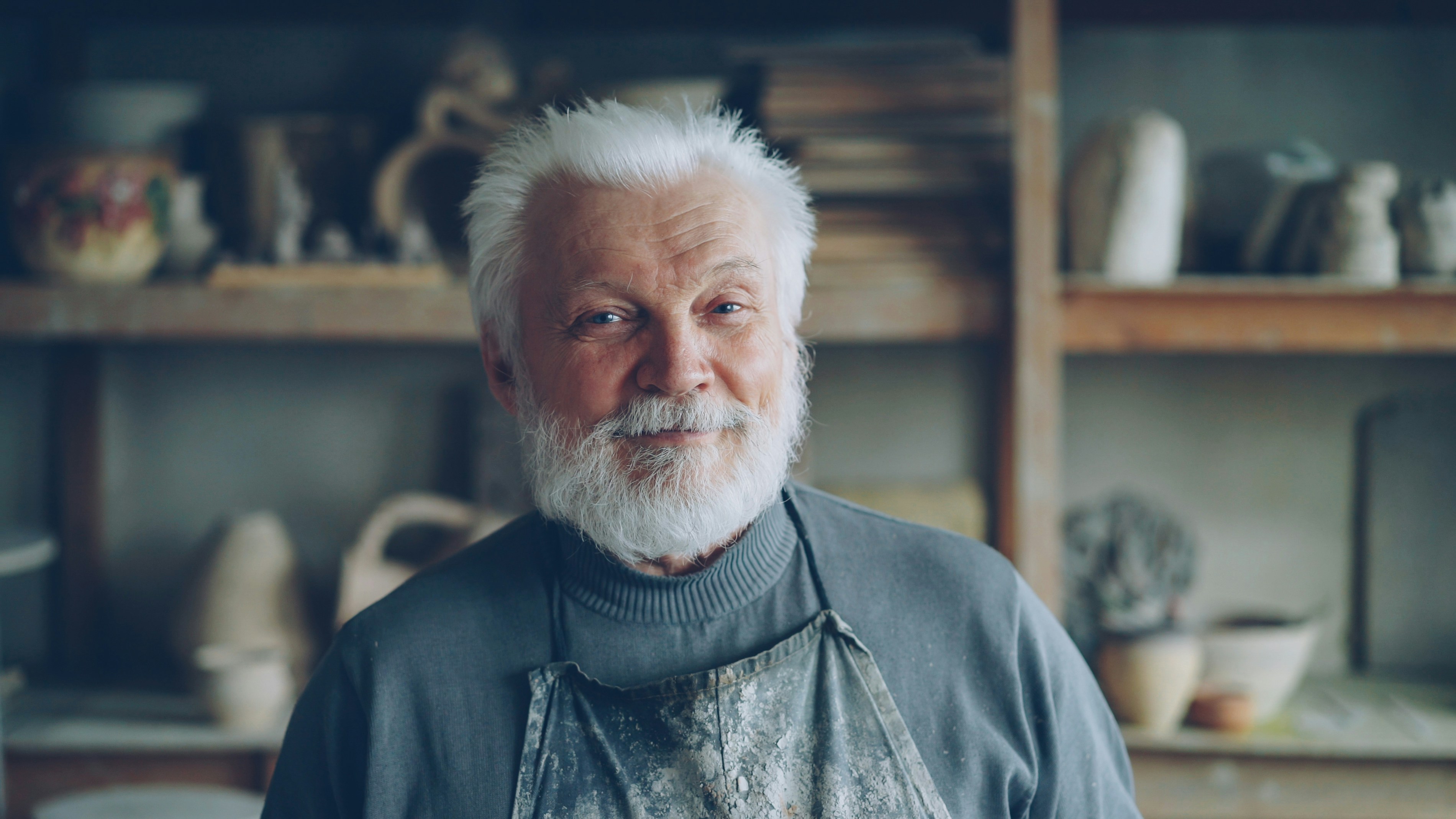 Close-up portrait of senior potter in muddy apron smiling