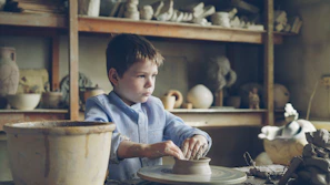 Boy sculpts a pot on a pottery wheel.