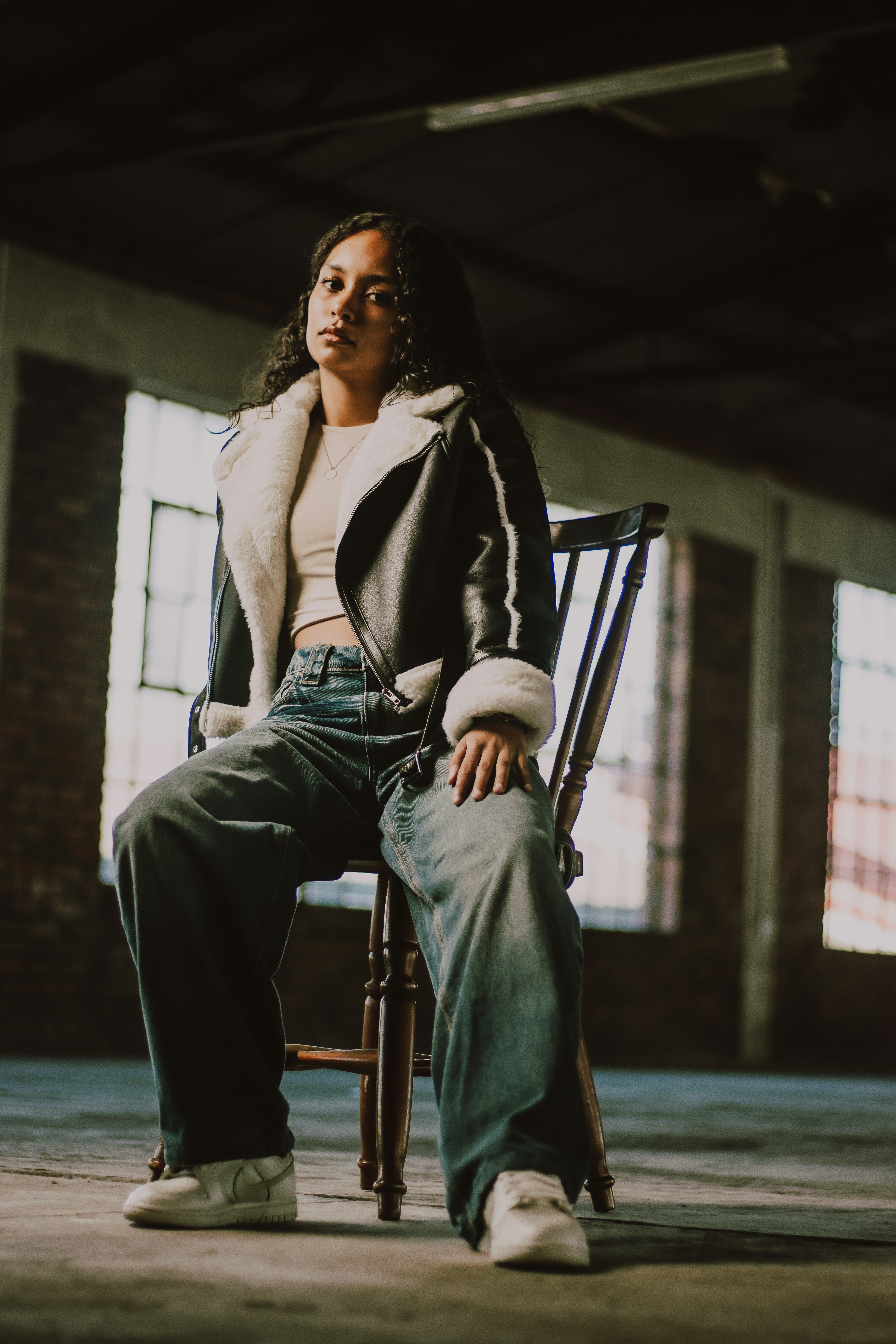 Eine junge Frau sitzt selbstbewusst auf einem Stuhl.