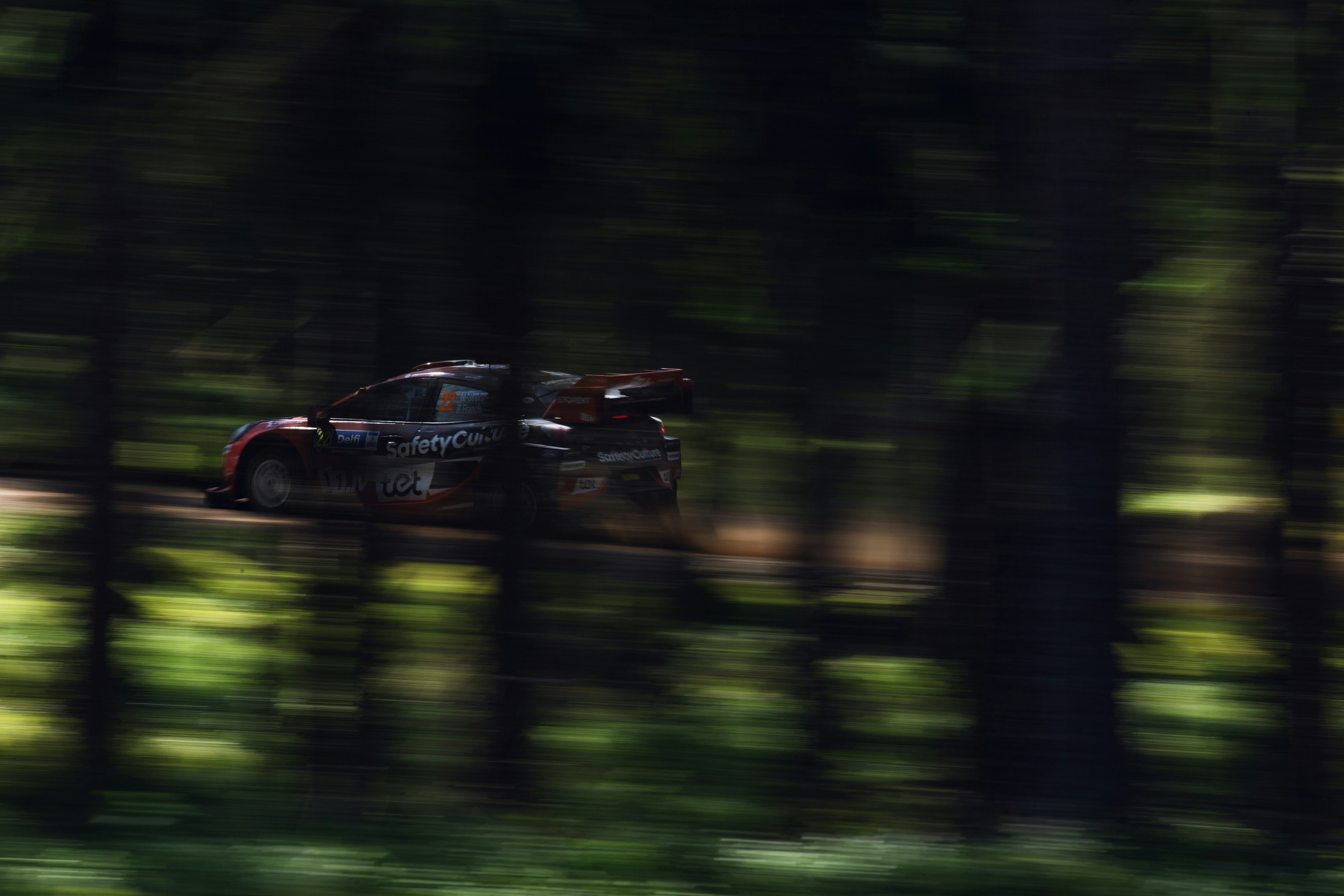 A rally car races through a forest.