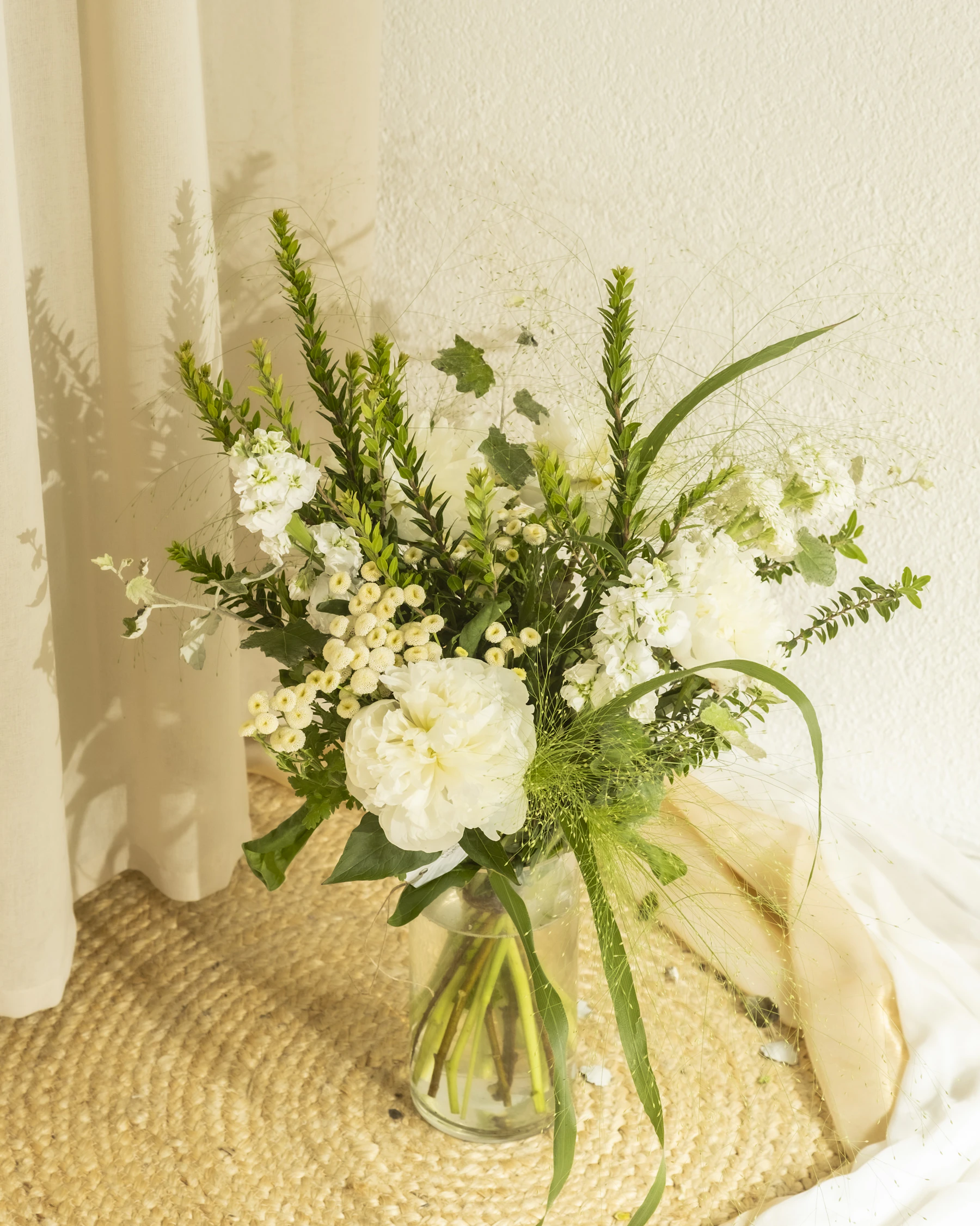 Soft white and green flower arrangement in a glass vase, warmly lit