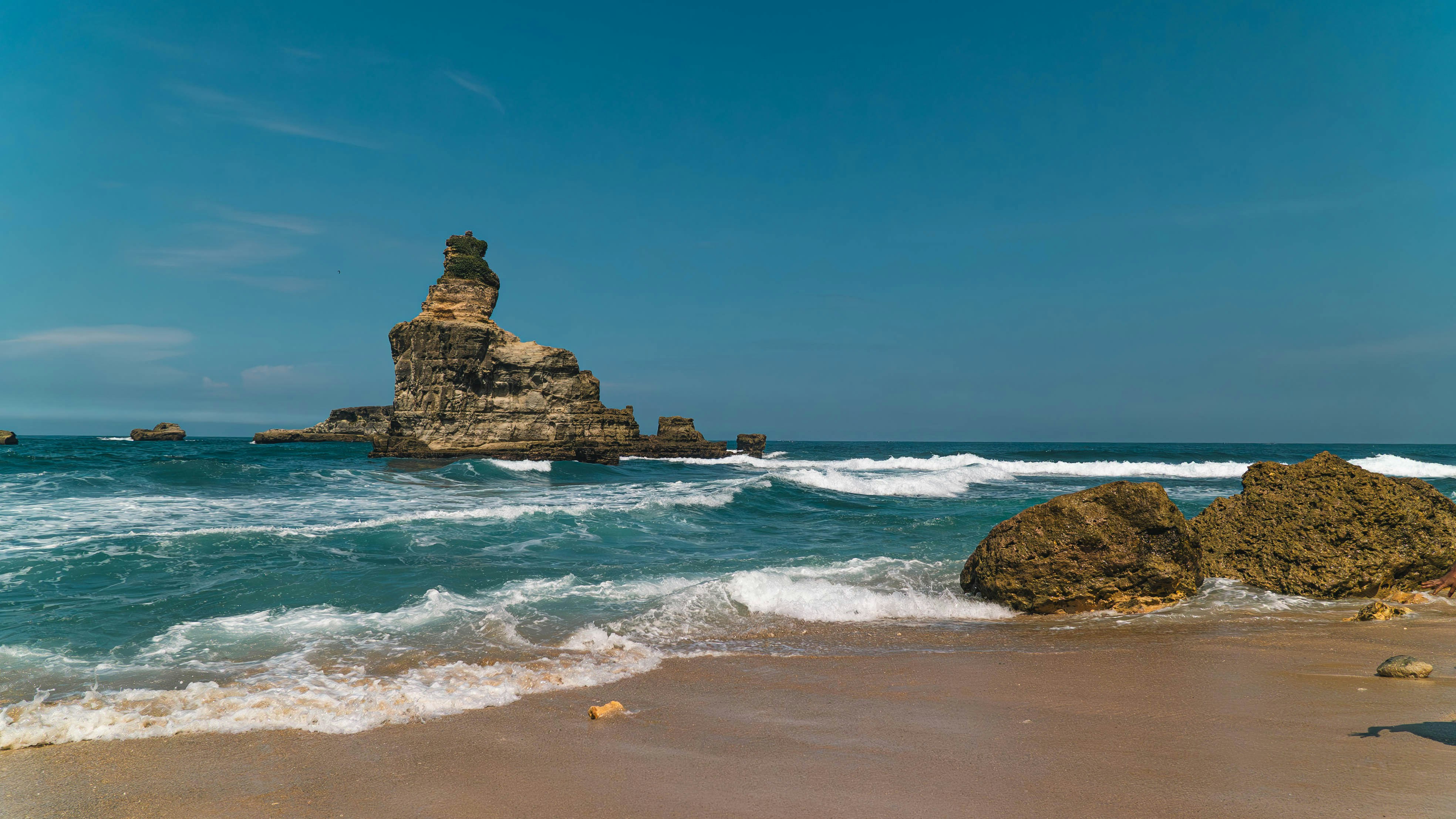 Waves crash on a sandy beach near rock formations.