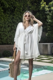 Woman poses in a white dress by the pool.
