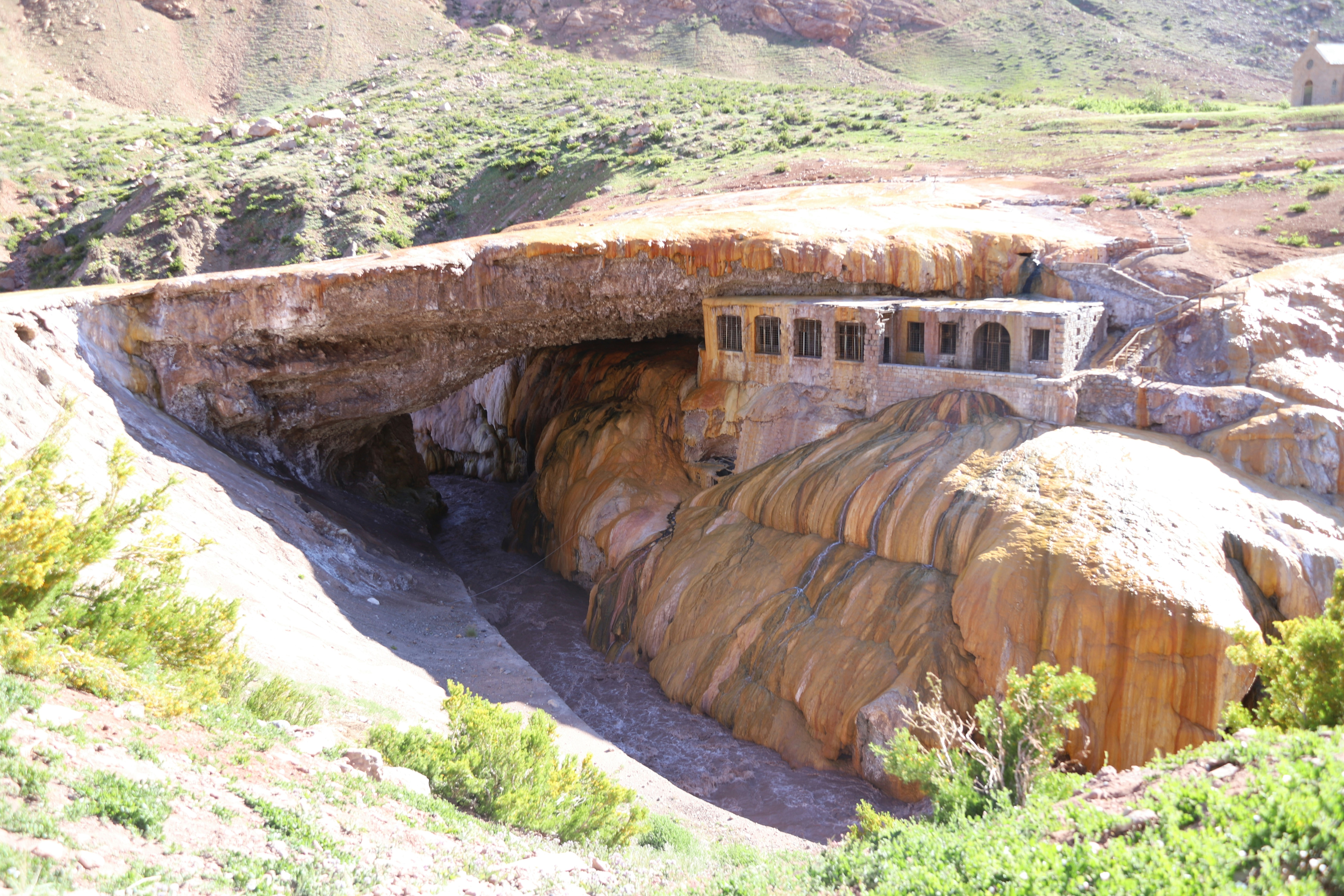 A natural bridge spans a canyon with a building.