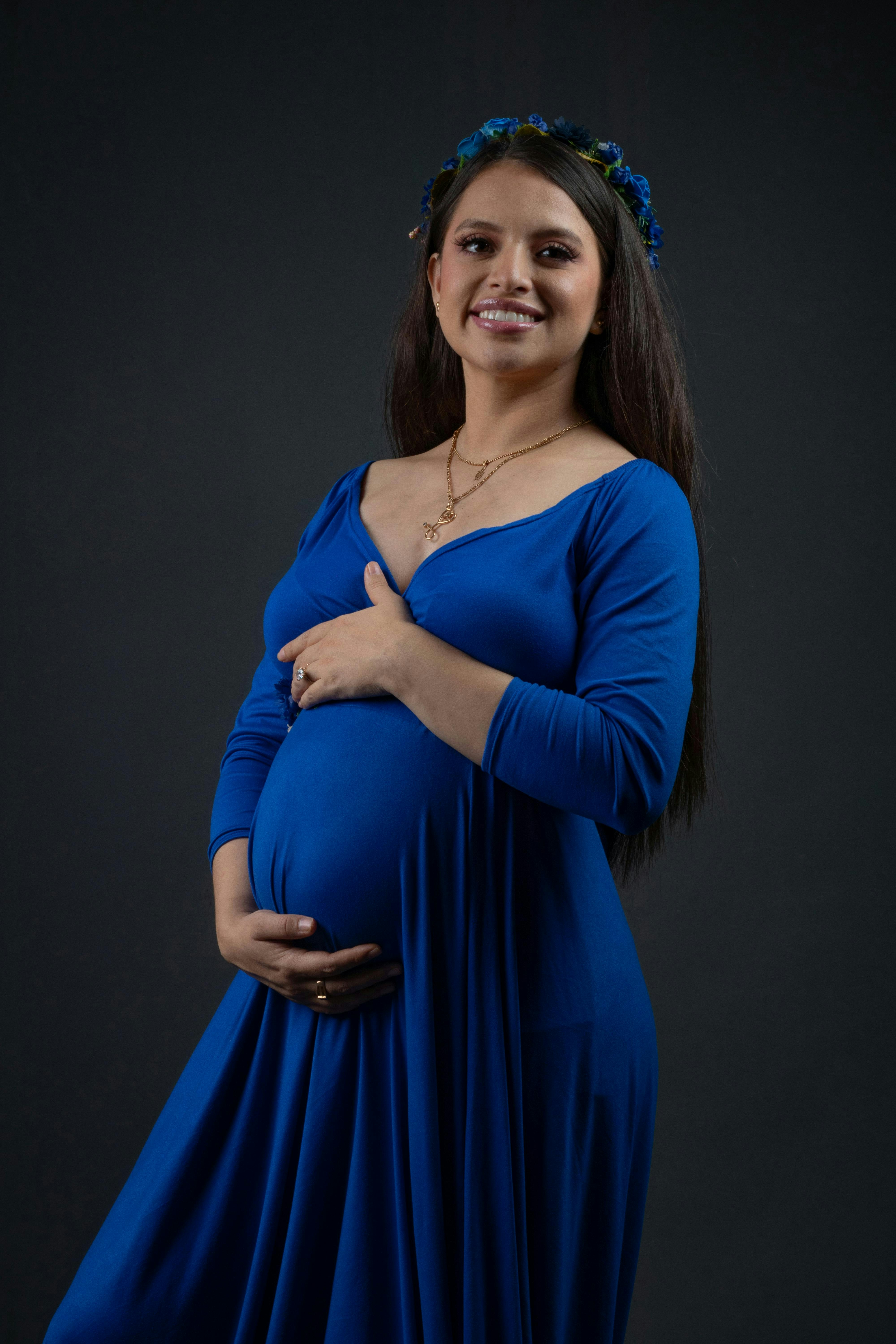 A pregnant woman poses smiling in a blue dress.